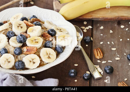 Warmes Frühstück der gesunden Hafermehl mit Pekannüssen, Bananen, Blaubeeren und Honig über eine rustikale Hintergrund. Bild geschossen von Overhead. Stockfoto