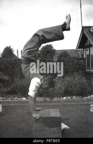 1950er Jahre, historische, junger Mann, Tragen von Kleidung, einen handstand auf einer Holzkiste außerhalb in einem Garten, England, UK. Stockfoto