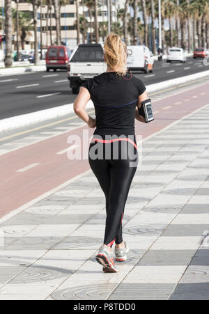 Ansicht der Rückseite des Weiblichen / Frau jogger Musik beim Joggen neben der geschäftigen Stadt Straße. Stockfoto