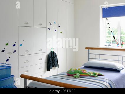 Blau gestreiften Abdeckung auf Holz und Metall Bett im modernen weißen Kind Schlafzimmer mit weißen vorhanden Abstellraum Stockfoto