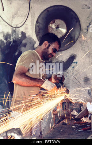 Türkischer Arbeitnehmer mit einem Winkelschleifer auf Metall in einen Arbeitsplatz. Stockfoto