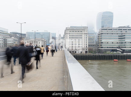 Montag morgen Pendler gehen auf die London Bridge über der Themse und gegenüber der City und Walkie Talkie Gebäude auf einem nebligen Tag arbeiten. Stockfoto