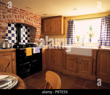 Schwarz Aga in gemauerten Kamin mit Blau + weiße Fliesen im Cottage Küche ausgestattet mit Holz Schränke und Blau + weiße Vorhänge Stockfoto