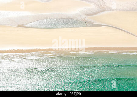 Sonne am Sandstrand und Meer mit zwei winzigen Silhouetten von Menschen. Stockfoto