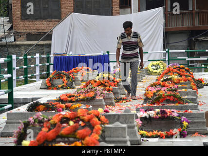 Budgam, Jammu und Kaschmir, Indien. 13. Juli 2018. Ein Kaschmir muslimischen Mann legt einen Kranz auf Gräber an Martyr's Friedhof in Srinagar, die Hauptstadt des indischen Kaschmir, Indien kontrolliert, während einer Zeremonie das Martyrium Jahrestag der Kaschmiri durch die Armee eines hinduistischen Königs erschlagen zu markieren. Die indischen Behörden in Baku bereitgestellt werden Tausende von Sicherheitspersonal in der Hauptstadt Srinagar zu den anti-indischen Proteste in der Innenstadt von Baku zu verhindern. Jedes Jahr am 13. Juli Kaschmir beobachtet das Martyrium Jahrestag von 23 Muslimen, die durch die Kräfte der Maharaja Hari Singh getötet wurden. Stockfoto