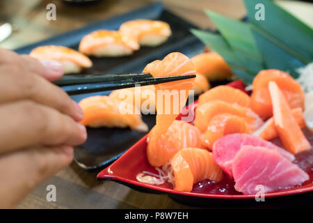 Stäbchen mit Lachs Sashimi mit gemischten geschnittenen Fisch sashimi auf Eis im schwarzen Schüssel. Japanisches Essen im asiatischen Restaurant. Stockfoto