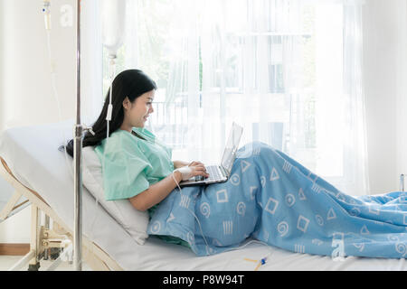 Asiatische Frau kranke Patient in einem Krankenhaus Bett liegend mit einem Laptop für entspannen, wenn Sie die Wiederherstellung für Kranke im Krankenhaus. Stockfoto