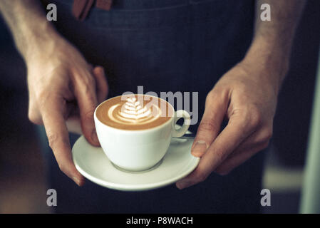 Barista serviert eine schöne flache Weiß mit Latte Art, mit den Händen in der Nähe Stockfoto