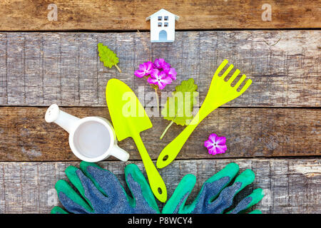 Flach mit Gartengeräte, Gießkanne, Schaufel, Spaten, Rechen, Handschuh, Blumen und Spielzeug Haus auf rustikalen Holzmöbeln Hintergrund. Im Frühling oder im Sommer im Garten Stockfoto