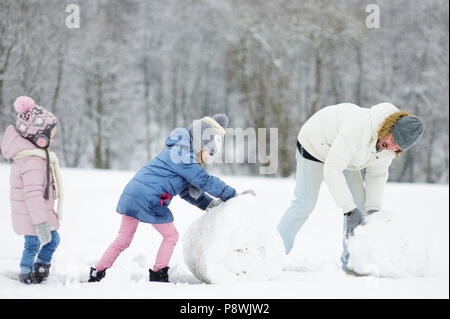 Junger Vater und zwei kleinen Schwestern gemeinsam einen Schneemann bauen in schönen Winter Park bei Schneefall Stockfoto