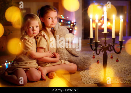 Glückliche kleine Mädchen sitzt vor dem Kamin in der gemütlichen dunklen Wohnzimmer am Heiligabend Stockfoto