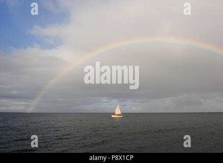 Eine kleine gaff manipulierten Segelboot Segel unter einem riesigen Regenbogen im Clyde Esturary, Scottand Stockfoto