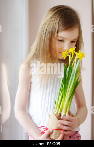 Bezaubernd lächelnde Mädchen Narzissen Holding durch die Fenster Stockfoto