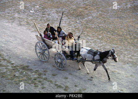 Von oben gesehen, eine türkische Familie mit Großeltern und Kindern dash entlang einer staubigen Strecke in einem hölzernen pony Warenkorb. Der Mann, der die Karre Wellen an der Kamera. Kappadokien, Türkei Stockfoto