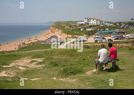 Paar auf Sitz mit Blick auf Urlauber auf Hive Strand Burton Bradstock Dorset UK Stockfoto