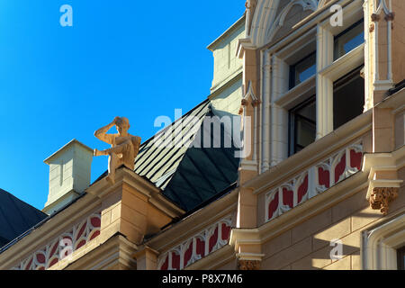 Skulptur eines Jungen mit einem Buch auf dem Dach eines alten Hauses mit Windows gegen die blauen Sommerhimmel. Riga, Lettland Stockfoto