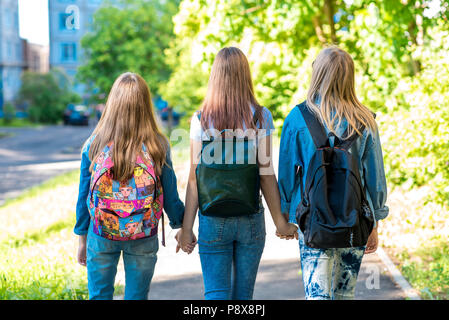Drei Mädchen Schülerin Freundinnen. Sie halten einander die Hände. Sommer in der Stadt. Ansicht von hinten. Sie gehen die Straße hinunter in die Schule. Rucksäcke hinter dem Rücken. Das Konzept ist die besten Freunde. Stockfoto