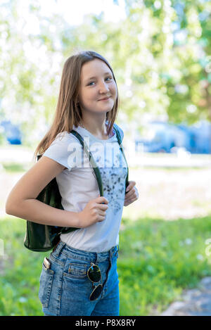 Mädchen Schulmädchen hinter Rucksack. Sommer in der Natur. Posieren vor der Kamera. Sie lächelt emotional. Stockfoto