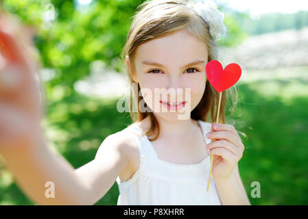 Adorable kleine Mädchen spielen mit Herz aus Papier auf einem Stock auf warmen Sommertag Stockfoto