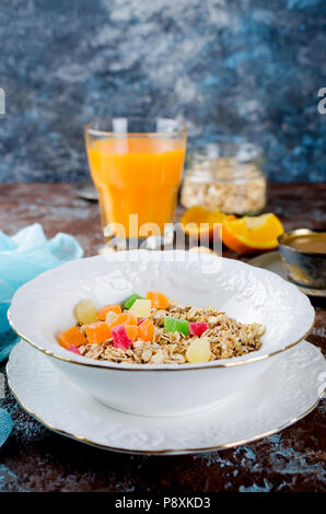 Gesundes Frühstück mit hausgemachtem Müsli in weiße Platte mit farbigen kandierte Früchte, Kaffee und Orangensaft auf dunklem Hintergrund. Kopieren Sie Platz Stockfoto