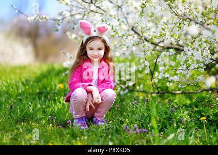 Adorable kleine Mädchen mit Hasenohren in Kirschblüten Garten auf schönen Frühlingstag Stockfoto