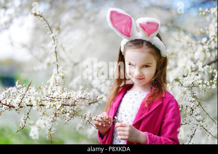 Adorable kleine Mädchen mit Hasenohren in Kirschblüten Garten auf schönen Frühlingstag Stockfoto