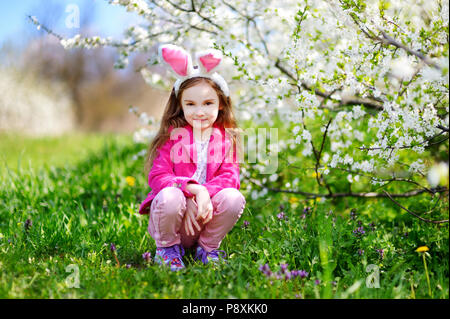 Adorable kleine Mädchen mit Hasenohren in Kirschblüten Garten auf schönen Frühlingstag Stockfoto