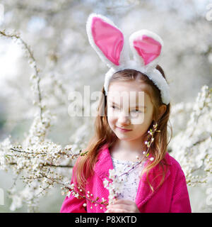 Adorable kleine Mädchen mit Hasenohren in Kirschblüten Garten auf schönen Frühlingstag Stockfoto