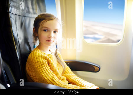 Entzückende kleine Mädchen mit dem Flugzeug reisen. Kind Flugzeug Fenster sitzen und nach draußen. Stockfoto