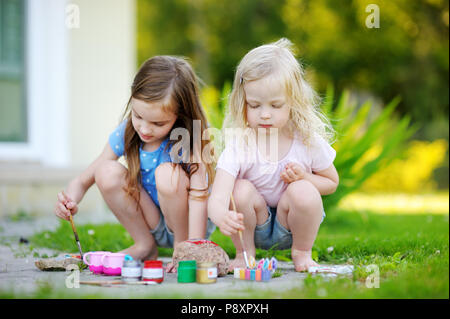 Zwei süße kleine Schwestern Malerei auf Steinen zusammen an einem heißen Sommertag Stockfoto