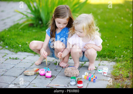 Zwei süße kleine Schwestern Malerei auf Steinen zusammen an einem heißen Sommertag Stockfoto