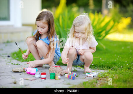 Zwei süße kleine Schwestern Malerei auf Steinen zusammen an einem heißen Sommertag Stockfoto