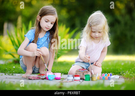 Zwei süße kleine Schwestern Malerei auf Steinen zusammen an einem heißen Sommertag Stockfoto