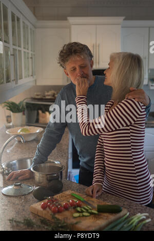 Ältere Frau füttern Mann beim Vorbereiten der Mahlzeiten in der Küche Stockfoto