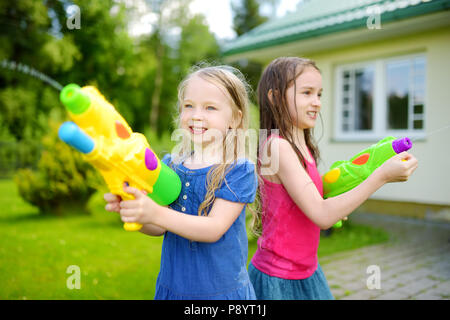 Adorable kleine Mädchen spielen mit Wasser Gewehren auf heißen Sommertag. Süße Kinder Spaß mit Wasser im Freien. Lustige Spiele für Kinder. Stockfoto