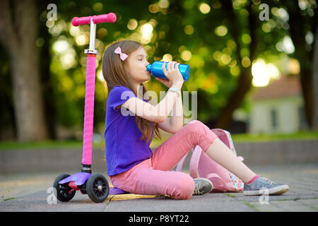 Kleines Kind lernen einen Roller in einem Stadtpark an sonnigen Sommerabend zu fahren. Süße kleine Mädchen reiten eine Rolle. Aktive Freizeit und Outdoor Sport für Stockfoto