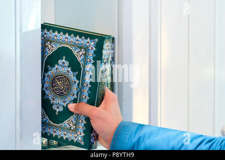 Des Menschen Hand eine Kopie des heiligen Qur'an aus einem Regal in dem weißen Inneren von Sultan Qaboos Grand Mosque in Maskat, Oman, Stockfoto