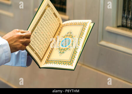 Kopie des heiligen Qur'an, die durch die Hände eines Mannes im weissen Innenraum der Sultan Qaboos Grand Mosque in Maskat, Oman, statt Stockfoto