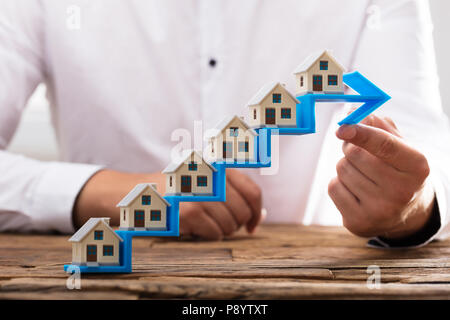 Nahaufnahme der Hand Haus Modelle ein Geschäftsmann auf Erhöhung der blaue Pfeil Treppe Stockfoto