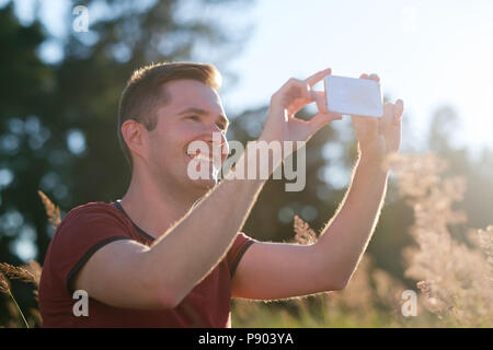 Junger Mann mit Handy in der Hand bei Sonnenuntergang, ein Foto der Natur am Telefon. Stockfoto