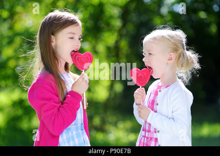 Zwei süße kleine Schwestern Essen großen herzförmigen Lutscher im Freien auf schönen Sommertag Stockfoto