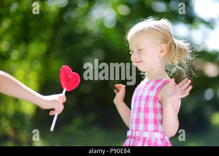 Süße kleine Mädchen mit großen herzförmigen Lollipop im Freien auf schönen Sommertag Stockfoto