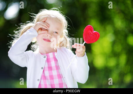 Süße kleine Mädchen mit großen herzförmigen Lollipop im Freien auf schönen Sommertag Stockfoto