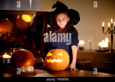 Adorable kleine Mädchen mit Halloween kostüm Spaß mit geschnitzten Kürbis im dunklen Zimmer an Halloween Stockfoto