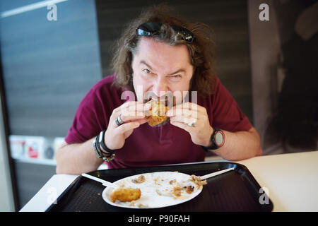 Lustig, bärtiger Mann sein Essen in Fast-Food-Restaurant genießen. Stockfoto