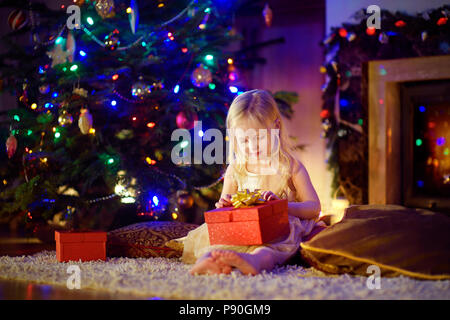 Happy girl Eröffnung zauberhafte Weihnachten Geschenk durch einen Kamin in der gemütlichen dunklen Wohnzimmer auf Heiligabend Stockfoto