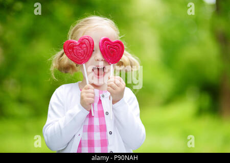 Süße kleine Mädchen mit großen herzförmigen Lollipop im Freien auf schönen Sommertag. Kind mit Lolly candy draußen. Stockfoto