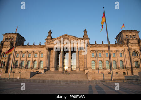 Das im Sonnenlicht eingetauchte Reichstagsgebäude in Berlin mit seiner großen neoklassizistischen Fassade und deutschen Fahnen davor. Stockfoto