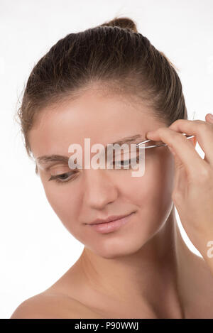 Junge schöne Mädchen zieht ihre Augenbrauen mit Pinzette aus Metall auf einem weißen Hintergrund Stockfoto