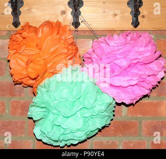 Bunte Papier pom poms hängen an Haken gegen eine Mauer. Stockfoto